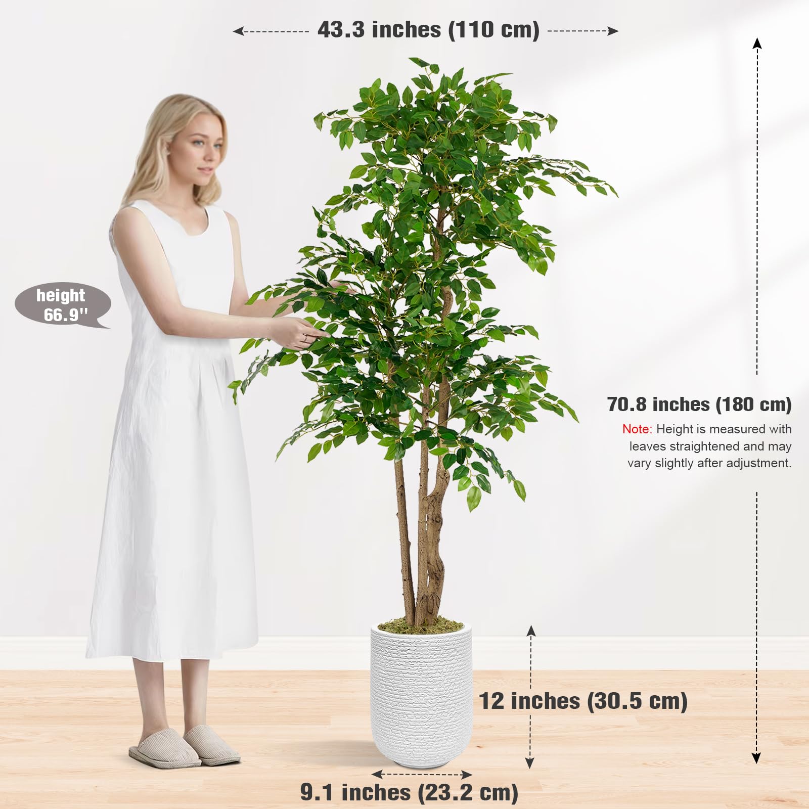 A 5.6FT artificial banyan tree in a white plastic pot placed in a living room setting, with a couch and window in the background.